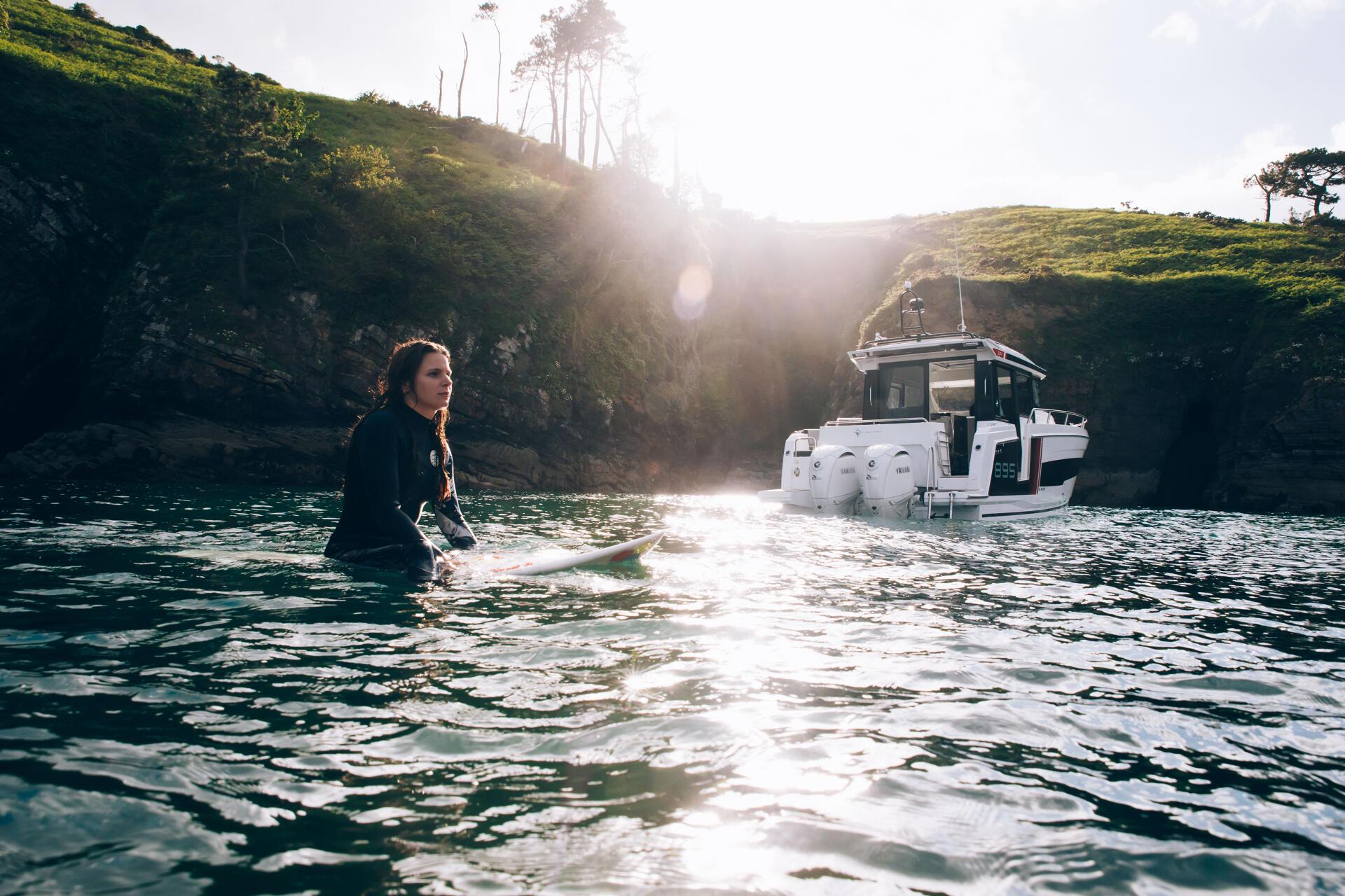 a woman on a surfboard in the water with a boat Merry fisher 895 S2 in the background